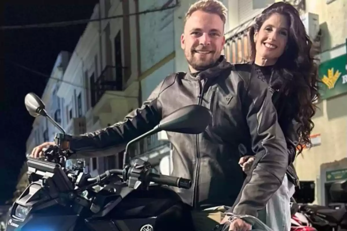 Una parella somrient en una motocicleta en un carrer il·luminat a la nit. Una parella somrient en una motocicleta en un carrer il·luminat a la nit.