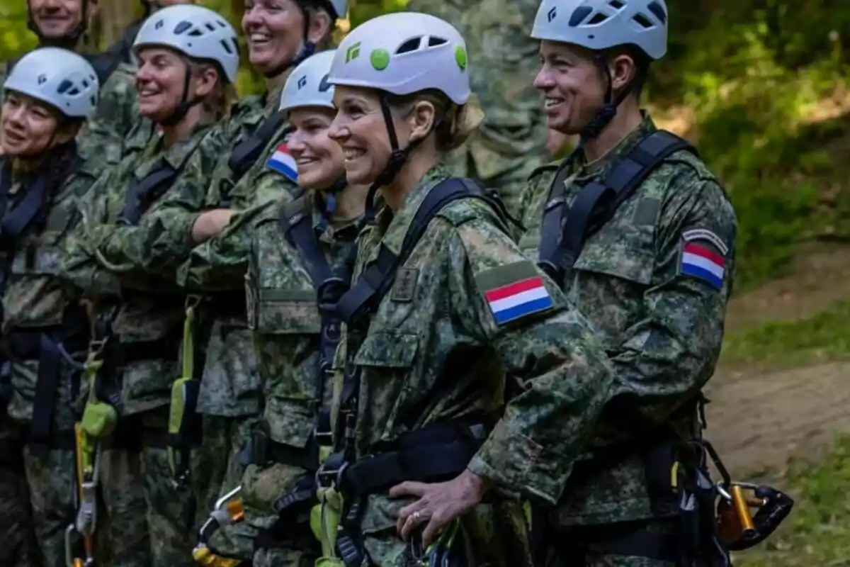 Un grup de persones amb uniformes de camuflatge i cascos blancs somriuen mentre estan dempeus en un entorn a l'aire lliure. Un grup de persones amb uniformes de camuflatge i cascos blancs somriuen mentre estan dempeus en un entorn a l'aire lliure.