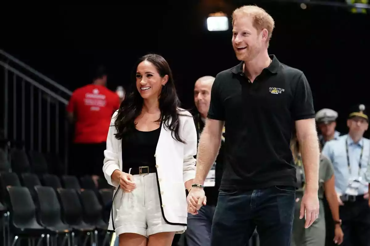 Una pareja sonriente camina de la mano en un evento deportivo con personas de fondo. Una pareja sonriente camina de la mano en un evento deportivo con personas de fondo.