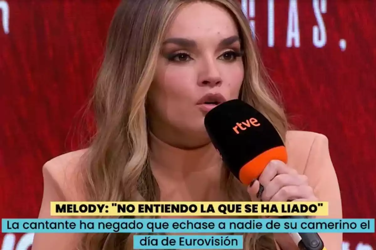 Dona amb els cabells llargs i rossos parlant en una entrevista mentre sosté un micròfon negre amb el logotip de rtve, sobre un fons vermell i amb subtítols a la part inferior. Dona amb els cabells llargs i rossos parlant en una entrevista mentre sosté un micròfon negre amb el logotip de rtve, sobre un fons vermell i amb subtítols a la part inferior.