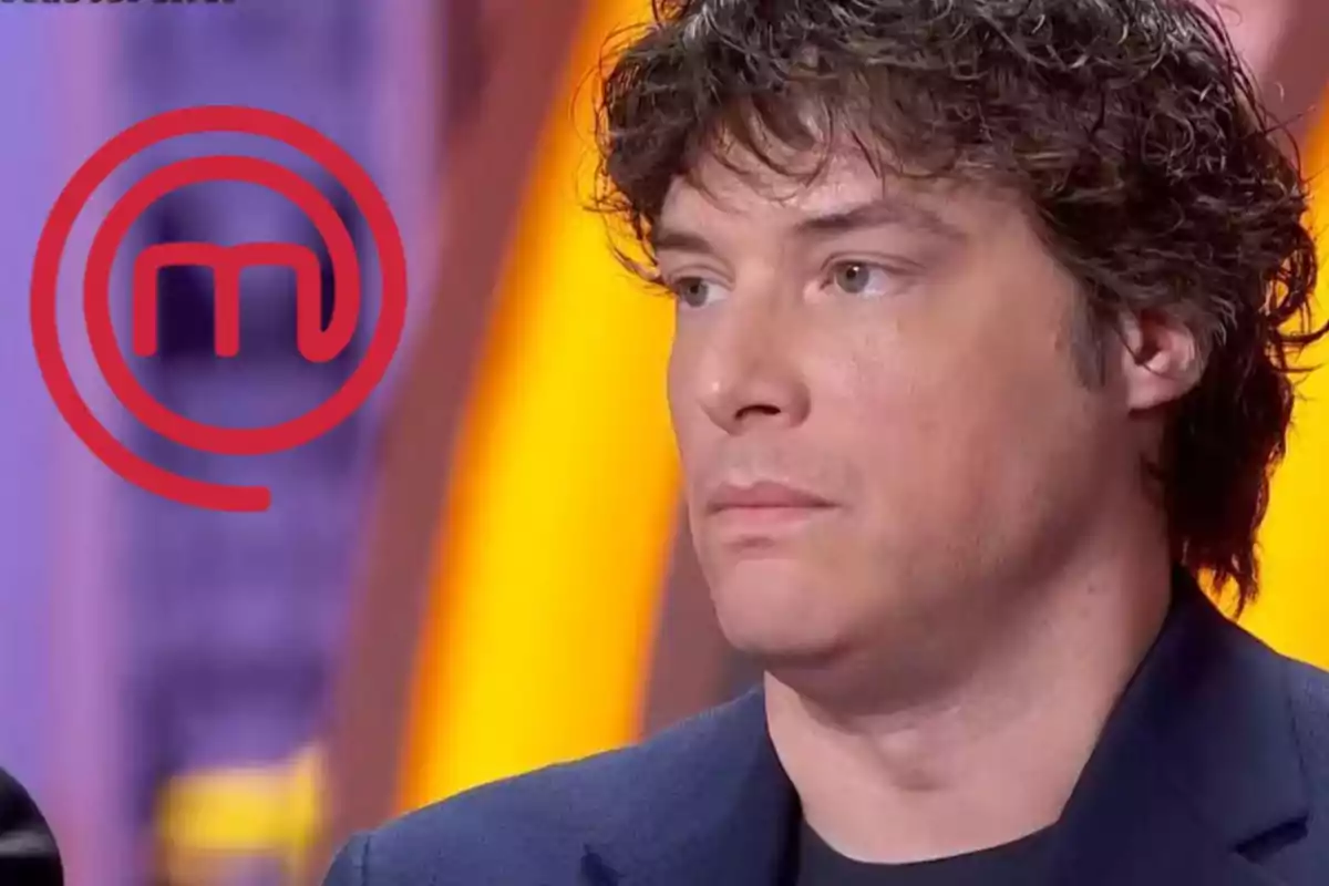 Un home amb expressió seriosa en un set de televisió amb el logotip de MasterChef al fons.