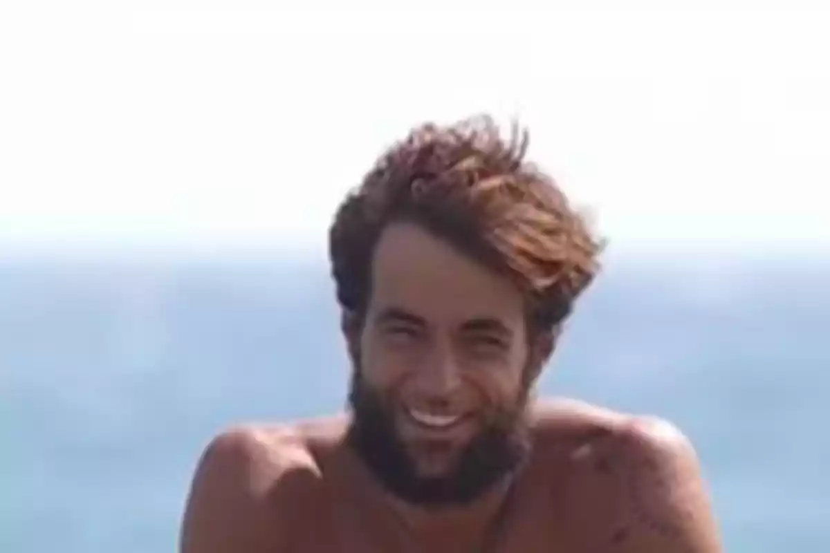 Home jove amb barba i cabells despentinats somrient davant del mar Home jove amb barba i cabells despentinats somrient davant del mar