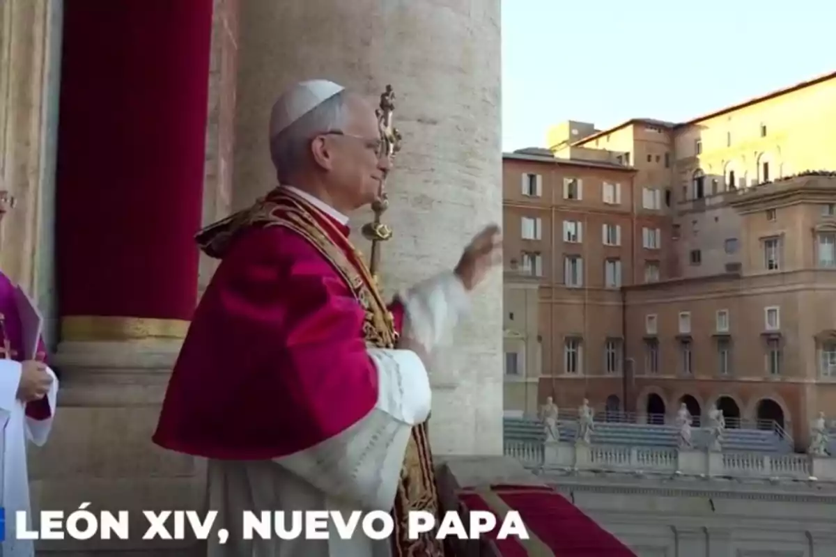 Un home vestit amb indumentària papal saluda des d'un balcó amb un edifici històric de fons. Un home vestit amb indumentària papal saluda des d'un balcó amb un edifici històric de fons.