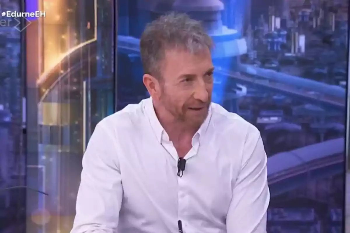 Un home amb camisa blanca està parlant en un programa de televisió amb un fons urbà il·luminat. Un home amb camisa blanca està parlant en un programa de televisió amb un fons urbà il·luminat.