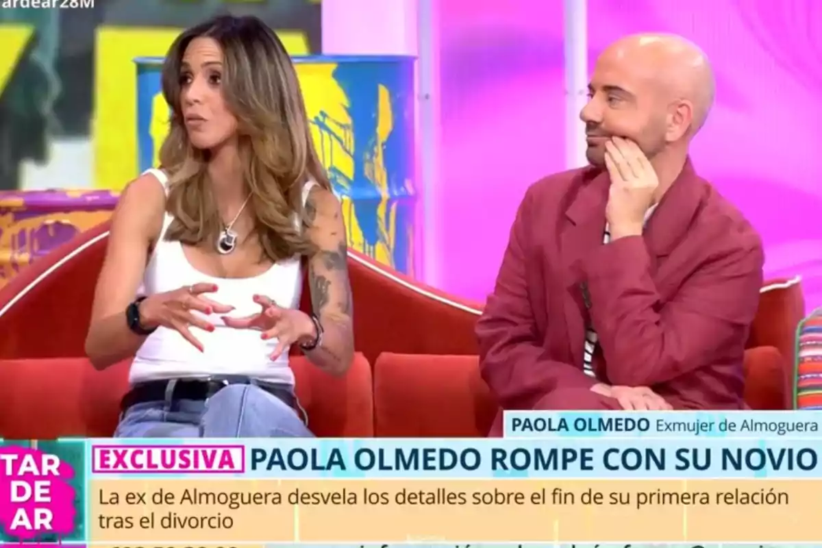 Dues persones assegudes en un sofà durant un programa de televisió, una dona amb samarreta blanca i un home amb jaqueta vermella conversen mentre a la pantalla apareix un titular sobre una ruptura amorosa. Dues persones assegudes en un sofà durant un programa de televisió, una dona amb samarreta blanca i un home amb jaqueta vermella conversen mentre a la pantalla apareix un titular sobre una ruptura amorosa.