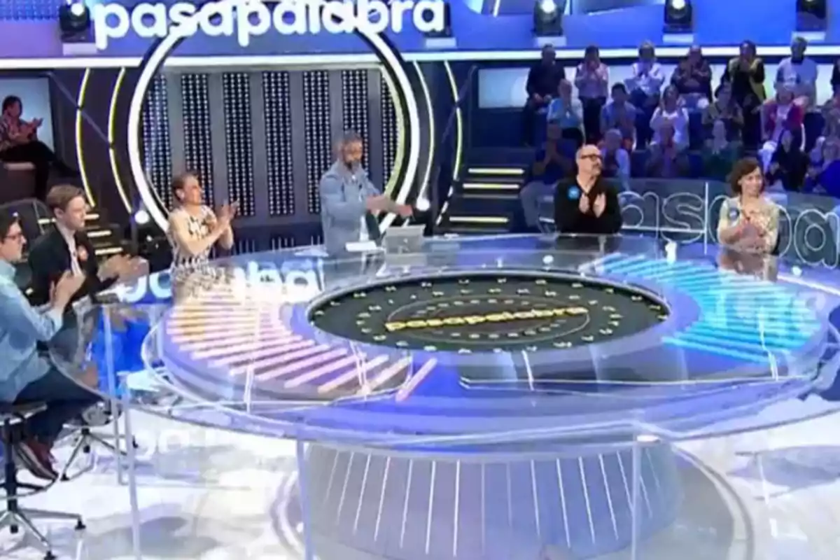 Un grup de persones aplaudeix en un plató de televisió amb un disseny circular i un públic al fons. Un grup de persones aplaudeix en un plató de televisió amb un disseny circular i un públic al fons.