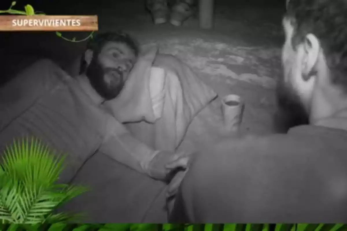 Pelayo y Joshua conversan en un entorno nocturno mientras Pelayo está recostado sobre una almohada improvisada, con un vaso al lado y rodeados de vegetación. Pelayo y Joshua conversan en un entorno nocturno mientras Pelayo está recostado sobre una almohada improvisada, con un vaso al lado y rodeados de vegetación.
