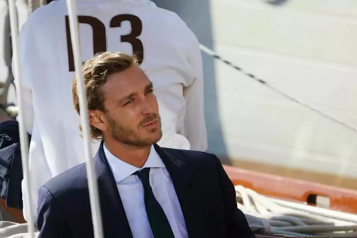 A man in a dark suit and tie is sitting outdoors, looking to the side with a thoughtful expression. A man in a dark suit and tie is sitting outdoors, looking to the side with a thoughtful expression.