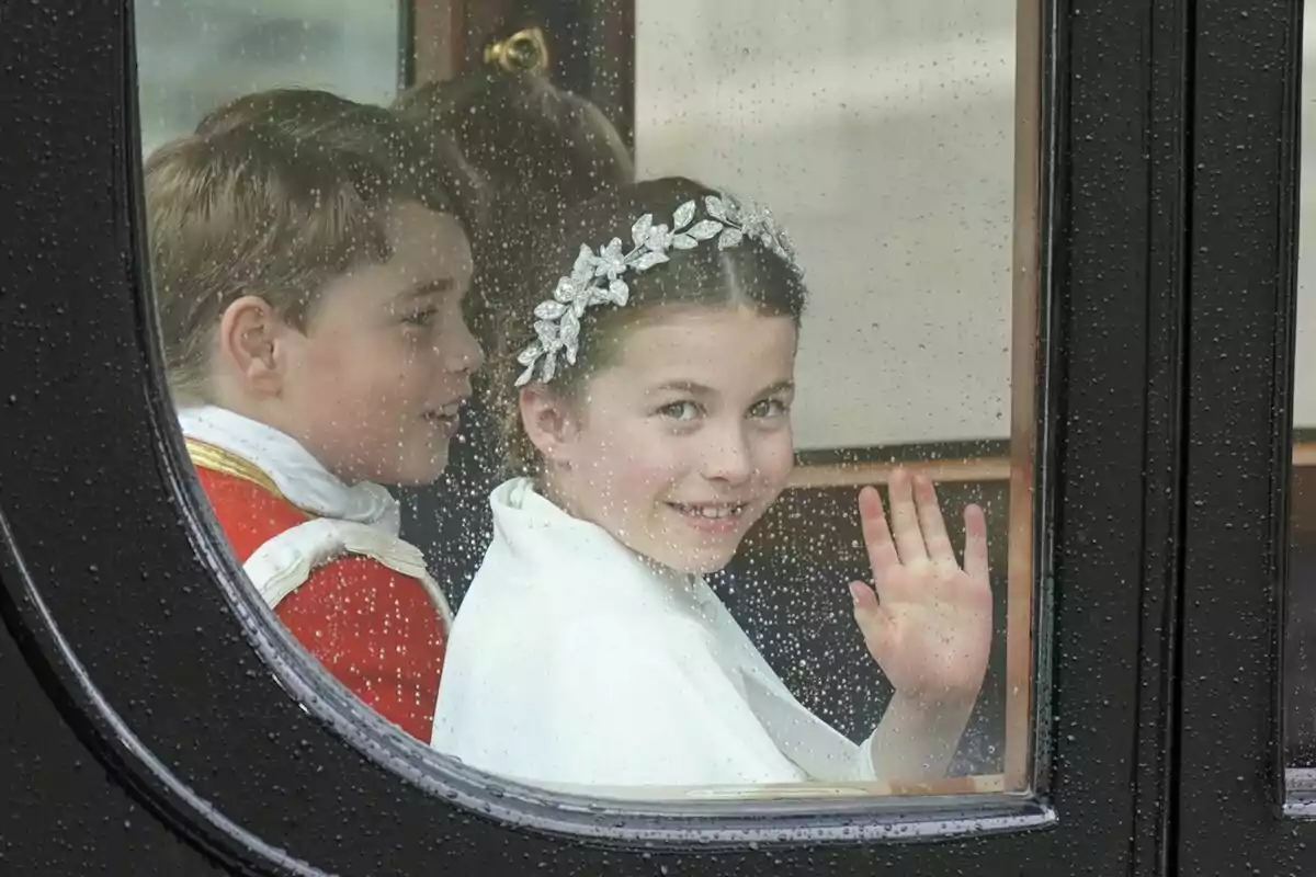 Two smiling children inside a carriage wave through a window with raindrops. Two smiling children inside a carriage wave through a window with raindrops.