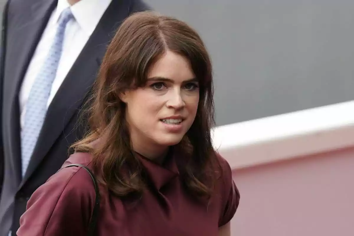 Brown-haired woman with loose hair wearing a burgundy blouse, walking outdoors next to a person in a dark suit Brown-haired woman with loose hair wearing a burgundy blouse, walking outdoors next to a person in a dark suit