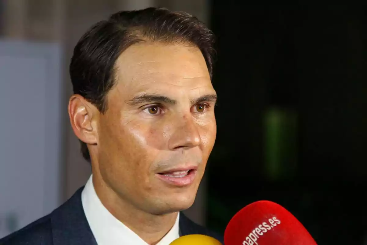 Hombre de cabello corto y oscuro vestido con traje hablando frente a varios micrófonos de colores