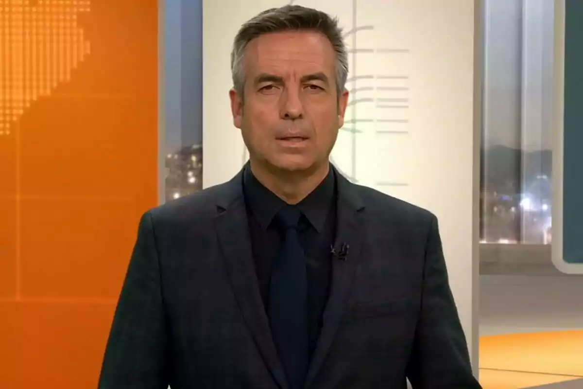 Un home amb vestit fosc i corbata blau fosc en un estudi de televisió amb fons taronja i blanc. Un home amb vestit fosc i corbata blau fosc en un estudi de televisió amb fons taronja i blanc.