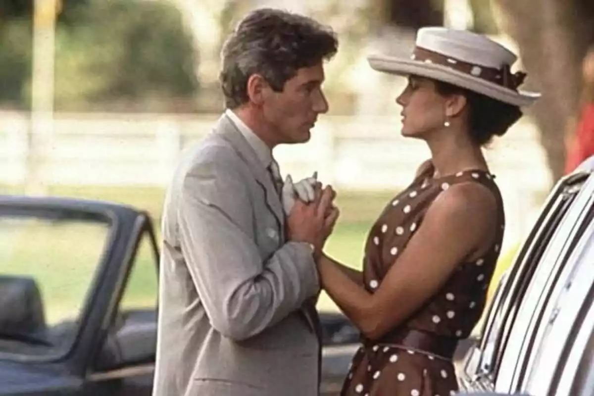 Elegantly dressed couple looks closely at each other and holds hands next to a convertible car in an outdoor setting. Elegantly dressed couple looks closely at each other and holds hands next to a convertible car in an outdoor setting.