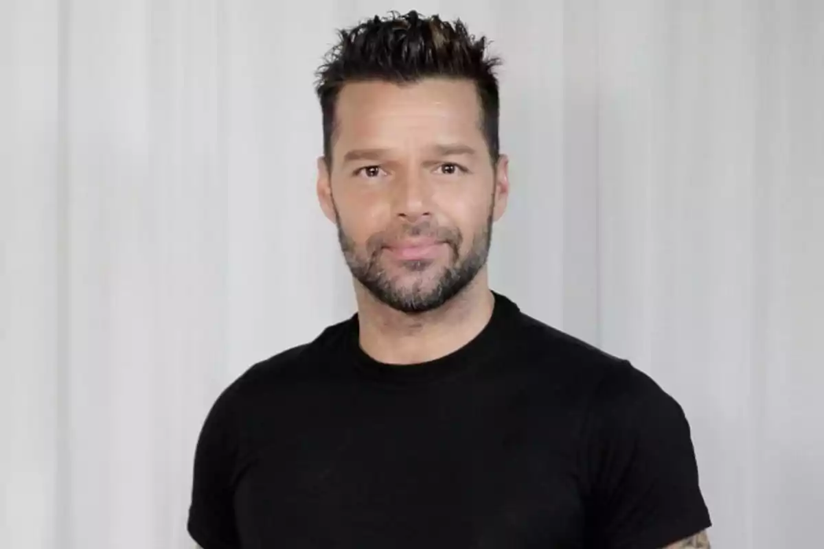 Ricky Martin with beard and short hair, wearing a black t-shirt, posing in front of a white curtain. Ricky Martin with beard and short hair, wearing a black t-shirt, posing in front of a white curtain.