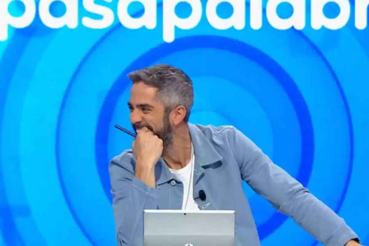 Home somrient i recolzat en un escriptori amb fons blau i lletres blanques. Home somrient i recolzat en un escriptori amb fons blau i lletres blanques.