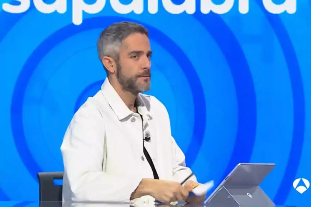 Un home amb barba i cabell curt canós està assegut davant d'un ordinador portàtil en un estudi de televisió amb un fons blau. Un home amb barba i cabell curt canós està assegut davant d'un ordinador portàtil en un estudi de televisió amb un fons blau.