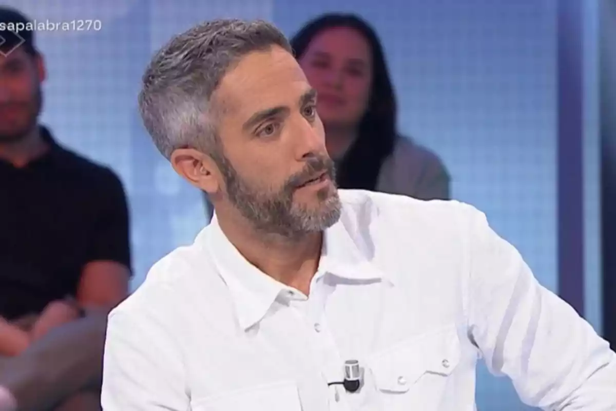 Un home amb barba i cabell canós porta una camisa blanca mentre està assegut en un estudi de televisió amb persones desenfocades al fons. Un home amb barba i cabell canós porta una camisa blanca mentre està assegut en un estudi de televisió amb persones desenfocades al fons.