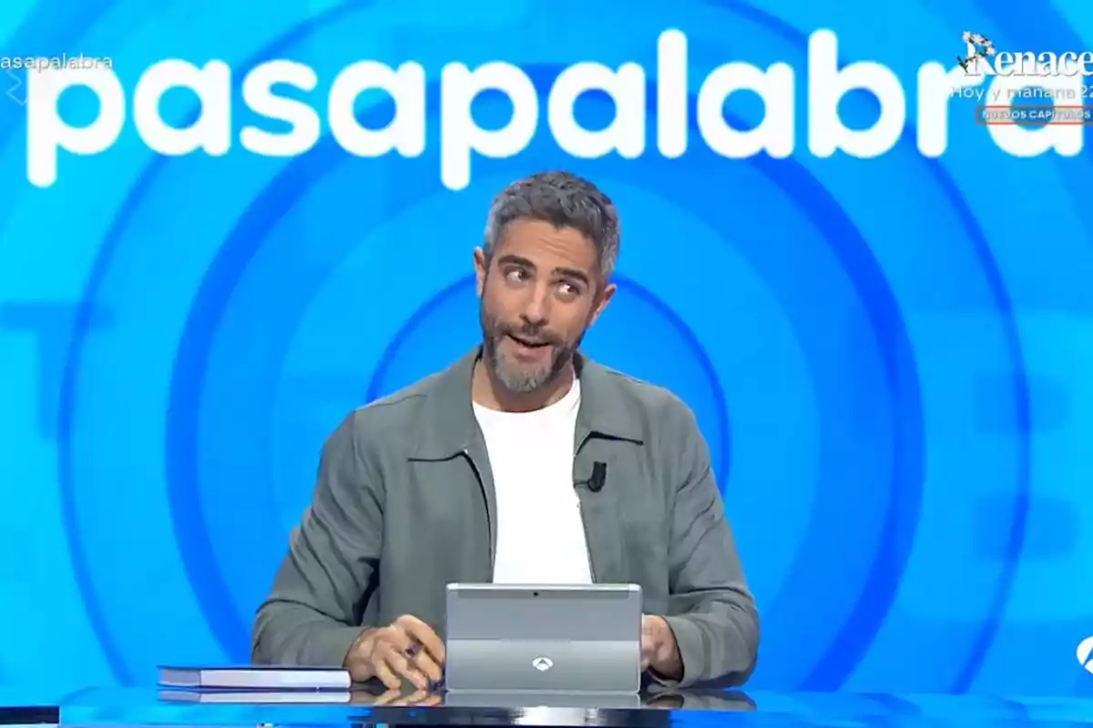 Un presentador de televisió està assegut davant d'una pantalla blava amb el logotip d'un programa de concursos. Un presentador de televisió està assegut davant d'una pantalla blava amb el logotip d'un programa de concursos.