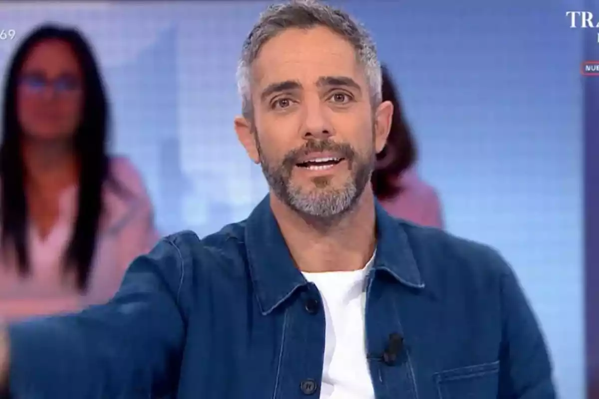 Un home amb barba i cabell curt canós, vestint una jaqueta blava i samarreta blanca, està parlant en un estudi de televisió amb un fons desenfocat. Un home amb barba i cabell curt canós, vestint una jaqueta blava i samarreta blanca, està parlant en un estudi de televisió amb un fons desenfocat.