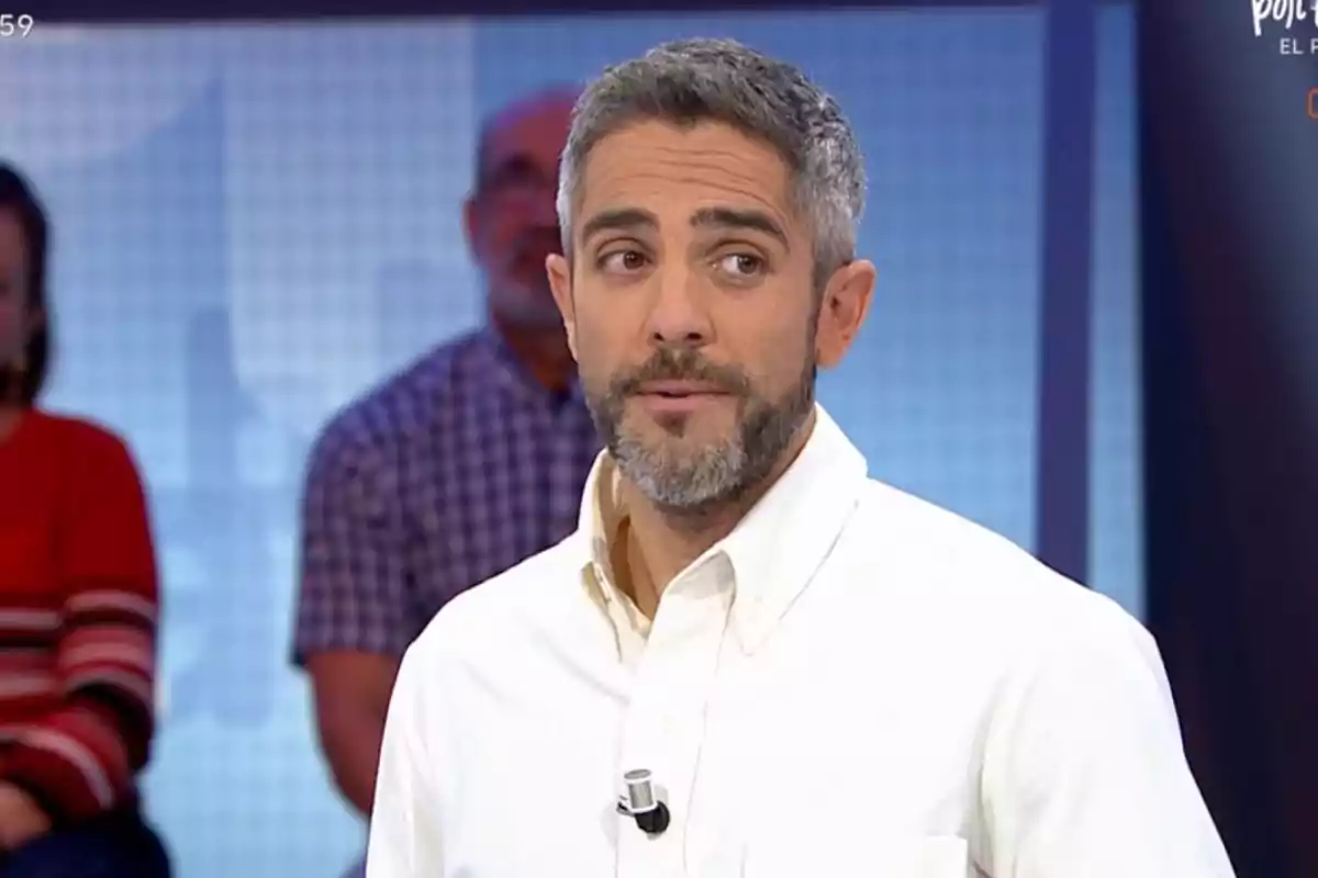 Un home amb barba i cabell canós, vestit amb camisa blanca, és en un estudi de televisió amb persones desenfocades al fons. Un home amb barba i cabell canós, vestit amb camisa blanca, és en un estudi de televisió amb persones desenfocades al fons.