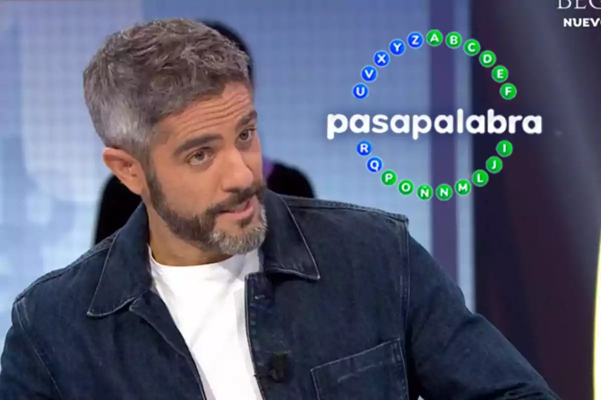 Un home amb barba i cabell canós està en un programa de televisió anomenat Pasapalabra amb un gràfic de lletres en cercle al seu costat.