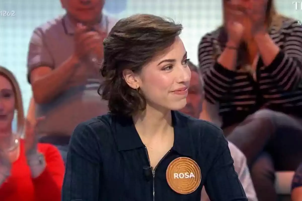 Una dona amb cabell castany i curt, vestida amb una jaqueta fosca i un distintiu que diu Una dona amb cabell castany i curt, vestida amb una jaqueta fosca i un distintiu que diu