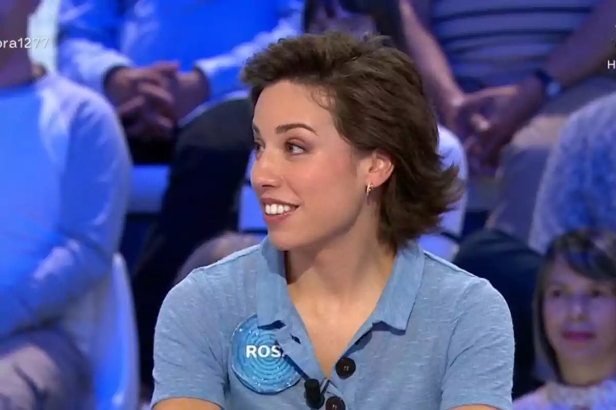 Dona jove amb cabell curt i castany, vestida amb una camisa blau clar i una placa amb el nom Dona jove amb cabell curt i castany, vestida amb una camisa blau clar i una placa amb el nom