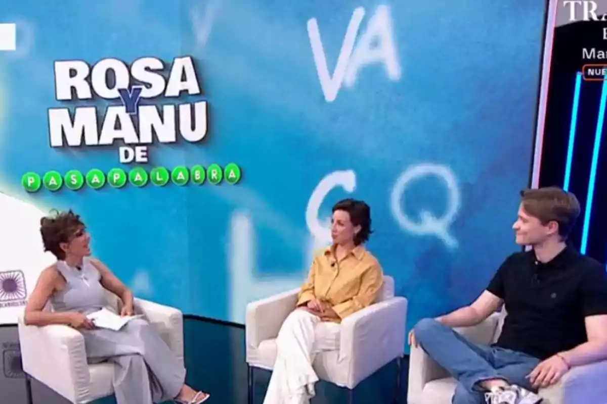Tres persones assegudes en butaques blanques conversen en un plató de televisió amb un fons blau que té lletres i el text ROSA I MANU DE PASAPALABRA. Tres persones assegudes en butaques blanques conversen en un plató de televisió amb un fons blau que té lletres i el text ROSA I MANU DE PASAPALABRA.