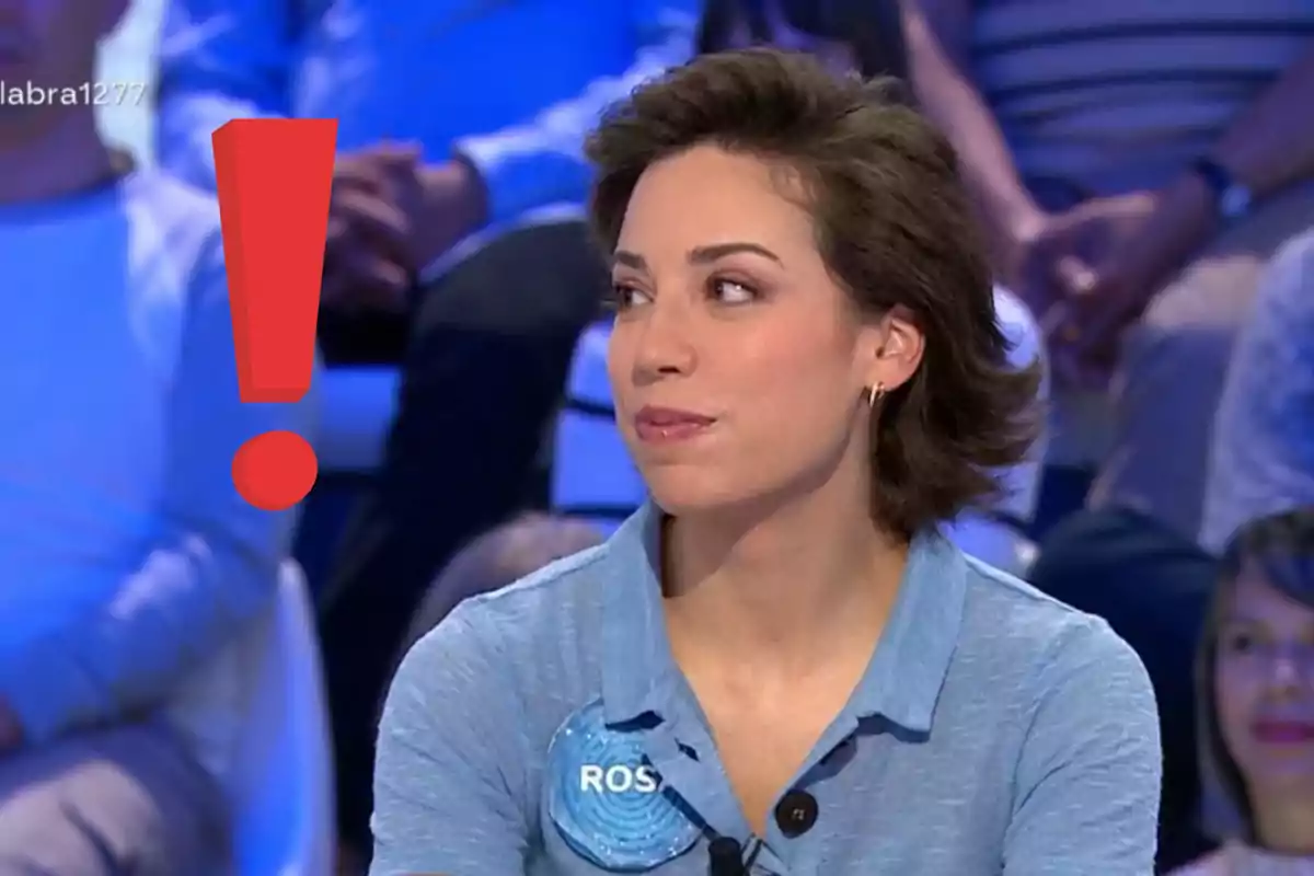 Dona amb camisa blau clar asseguda en un programa de televisió amb un gran signe d’exclamació vermell al seu costat