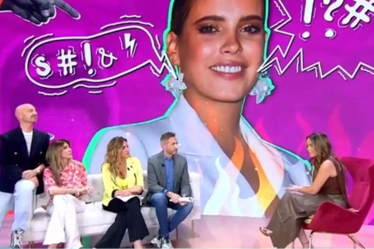 Un grup de persones està assegut en un plató de televisió amb un fons acolorit que mostra una imatge gran d'una dona somrient i gràfics de còmic. Un grup de persones està assegut en un plató de televisió amb un fons acolorit que mostra una imatge gran d'una dona somrient i gràfics de còmic.