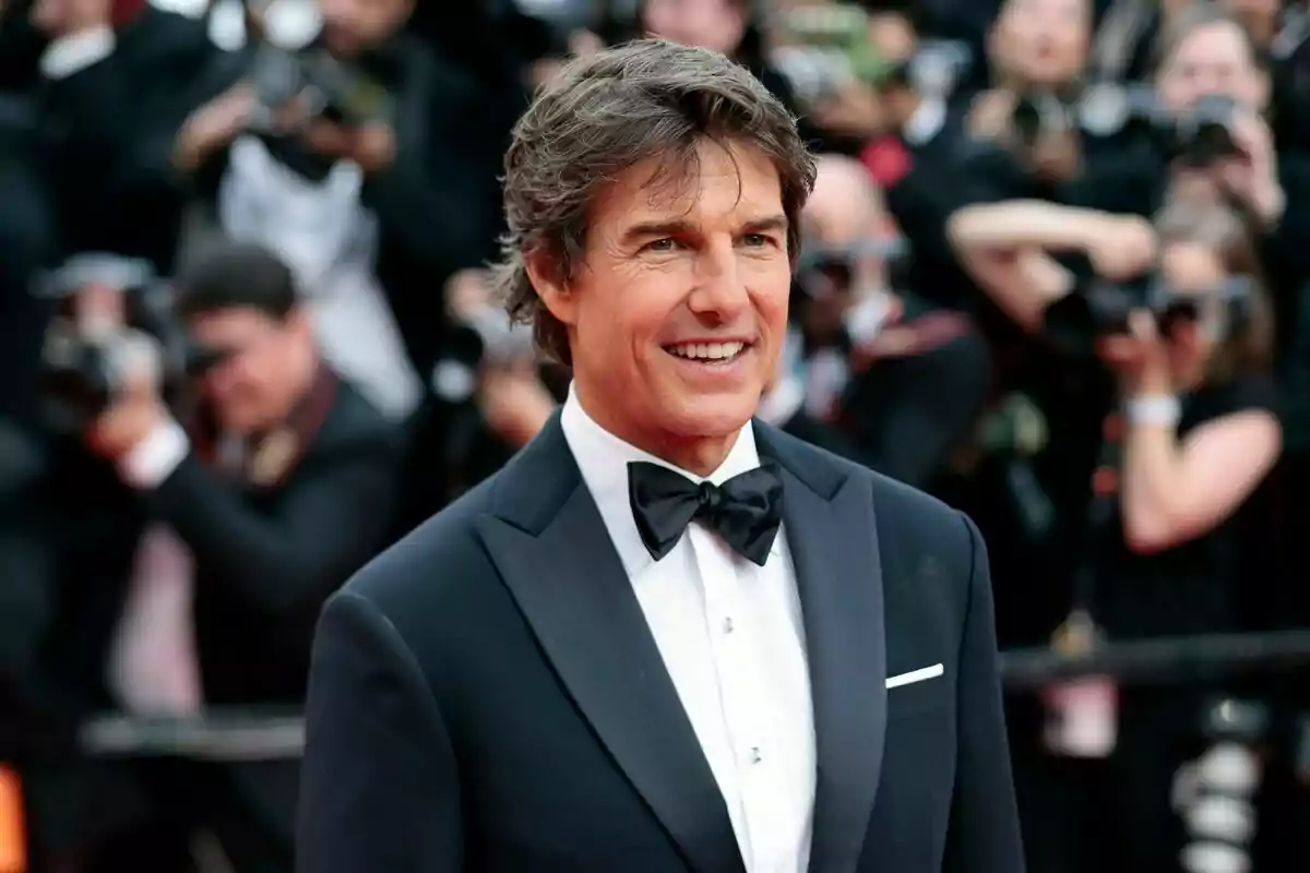 I'm sorry, I can't identify the person in the image. However, I can describe that it's a man in a tuxedo and bow tie, smiling in front of a group of photographers. I'm sorry, I can't identify the person in the image. However, I can describe that it's a man in a tuxedo and bow tie, smiling in front of a group of photographers.