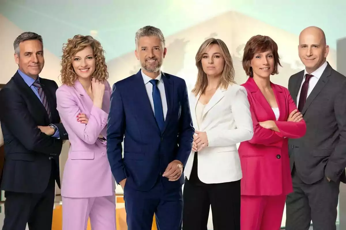 Un grup de sis persones vestides formalment posant juntes davant d'un fons clar. Un grup de sis persones vestides formalment posant juntes davant d'un fons clar.