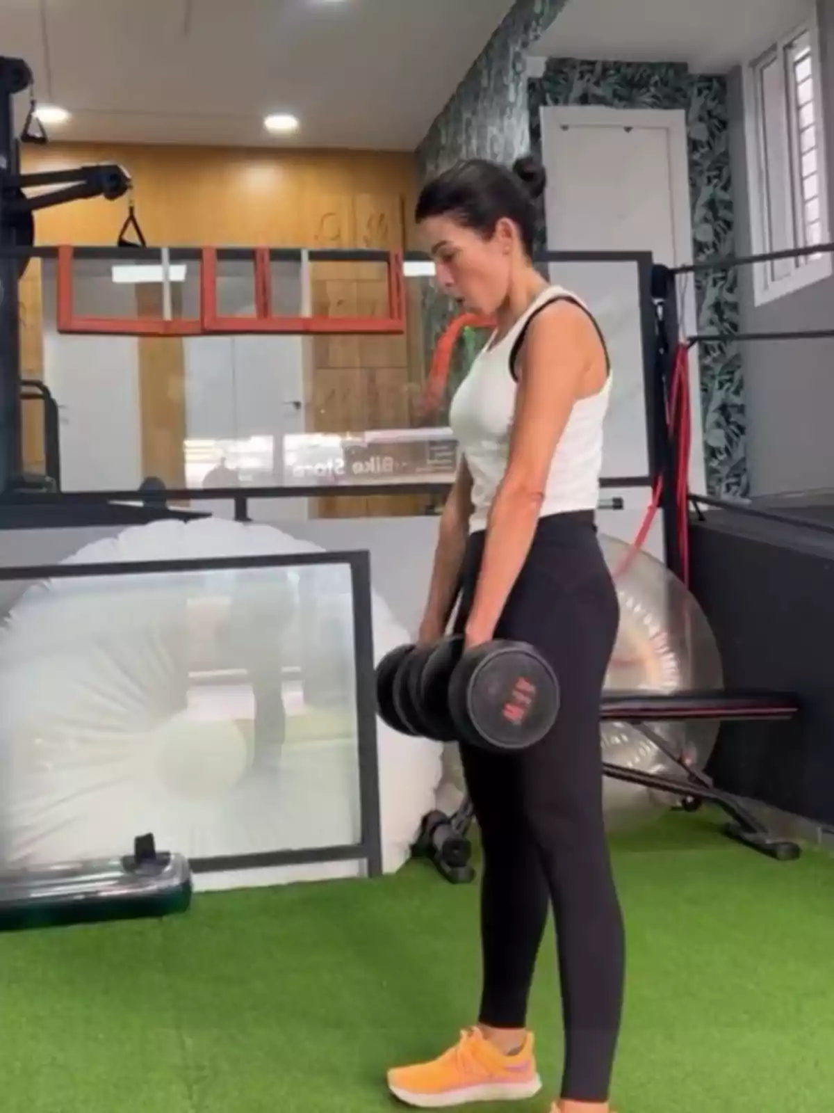 Una persona aixecant peses en un gimnàs amb terra de gespa artificial i equip d'exercici al fons. Una persona aixecant peses en un gimnàs amb terra de gespa artificial i equip d'exercici al fons.