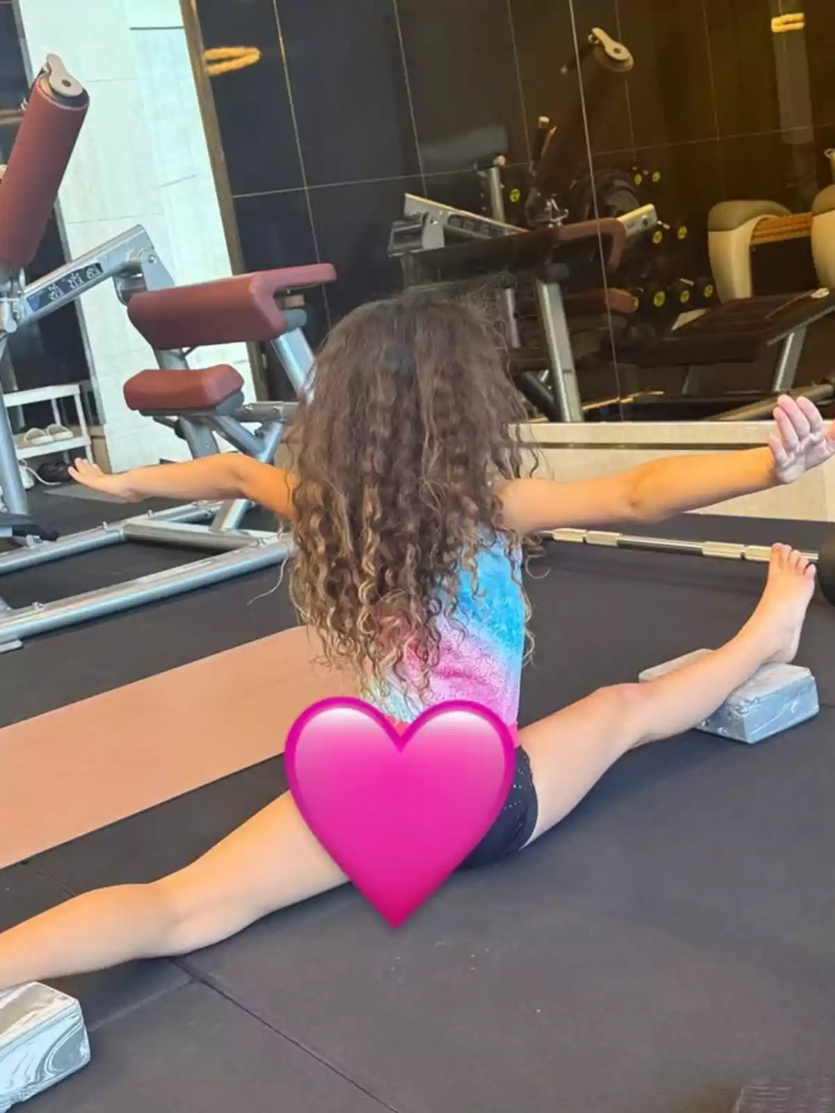 Girl doing a split on the gym floor with yoga blocks and a pink heart covering part of her body Girl doing a split on the gym floor with yoga blocks and a pink heart covering part of her body