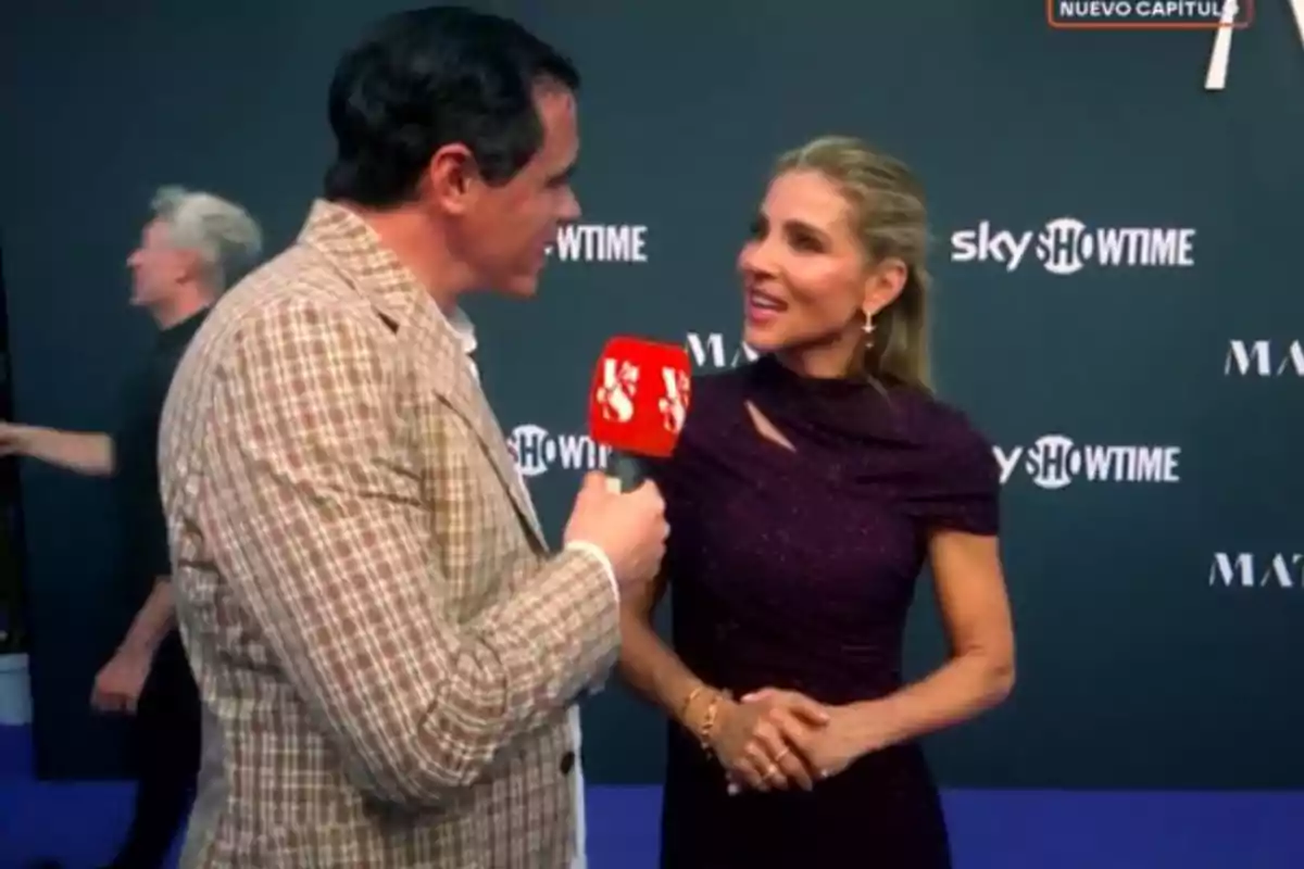 Un reporter entrevista una dona elegantment vestida en una catifa blava davant d’un fons amb logotips de SkyShowtime i altres patrocinadors.