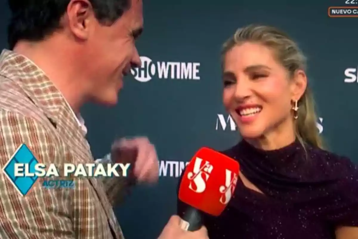 Una dona somriu mentre és entrevistada per un home en un esdeveniment amb un fons de logotips i un micròfon vermell.
