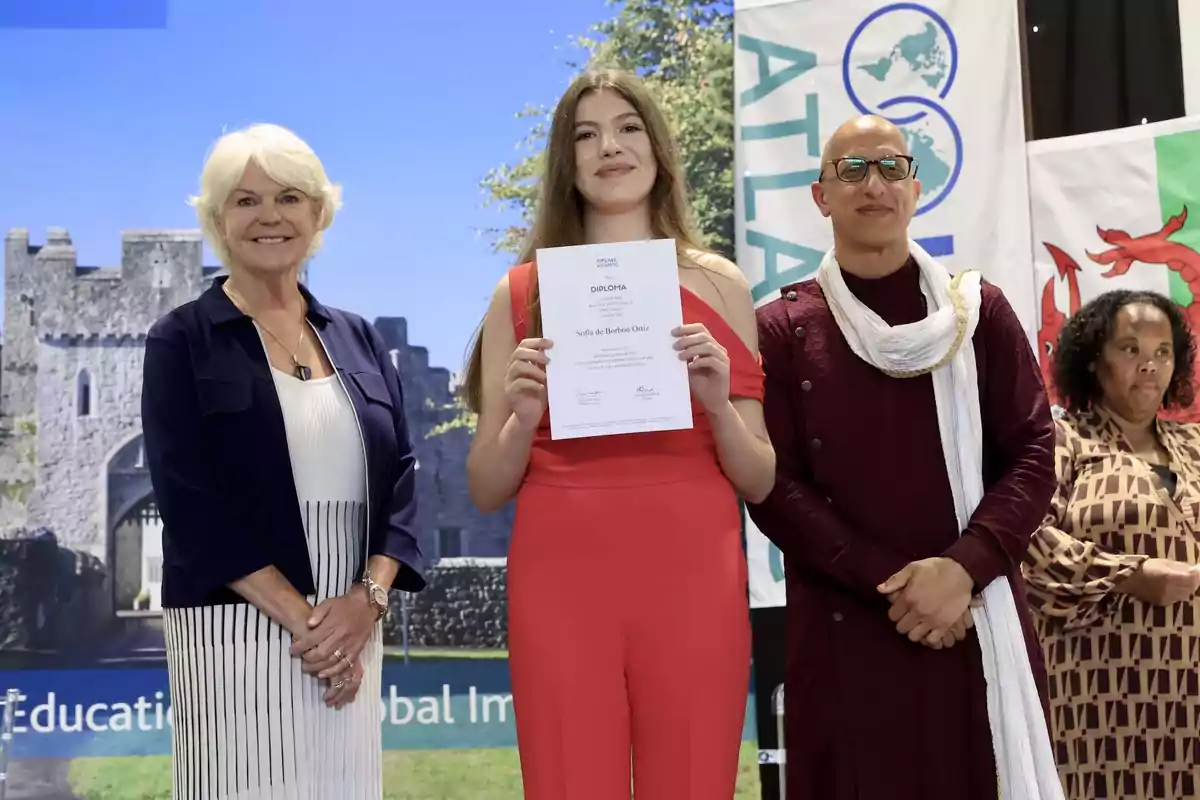 La infanta Sofia sosté un diploma mentre està dreta entre dues persones adultes, amb un fons de banderes i un castell. La infanta Sofia sosté un diploma mentre està dreta entre dues persones adultes, amb un fons de banderes i un castell.
