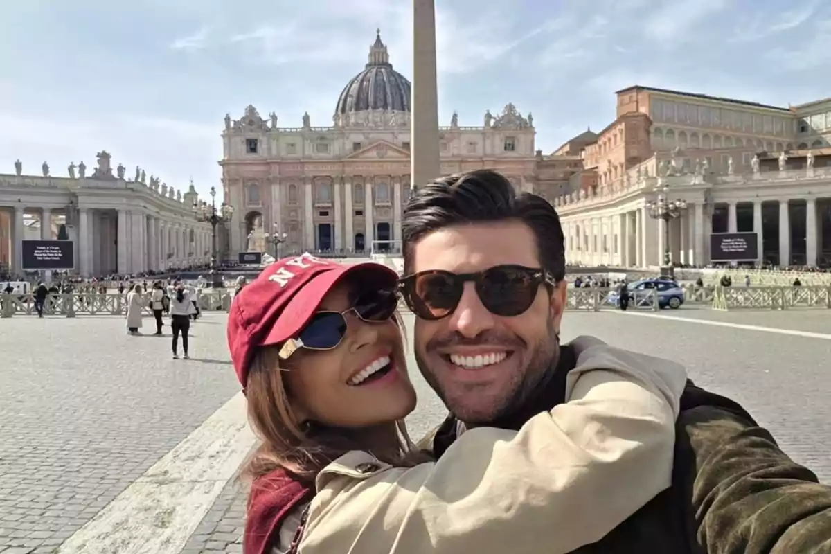 Una parella somrient es fa una selfie davant de la Basílica de Sant Pere al Vaticà en un dia assolellat.