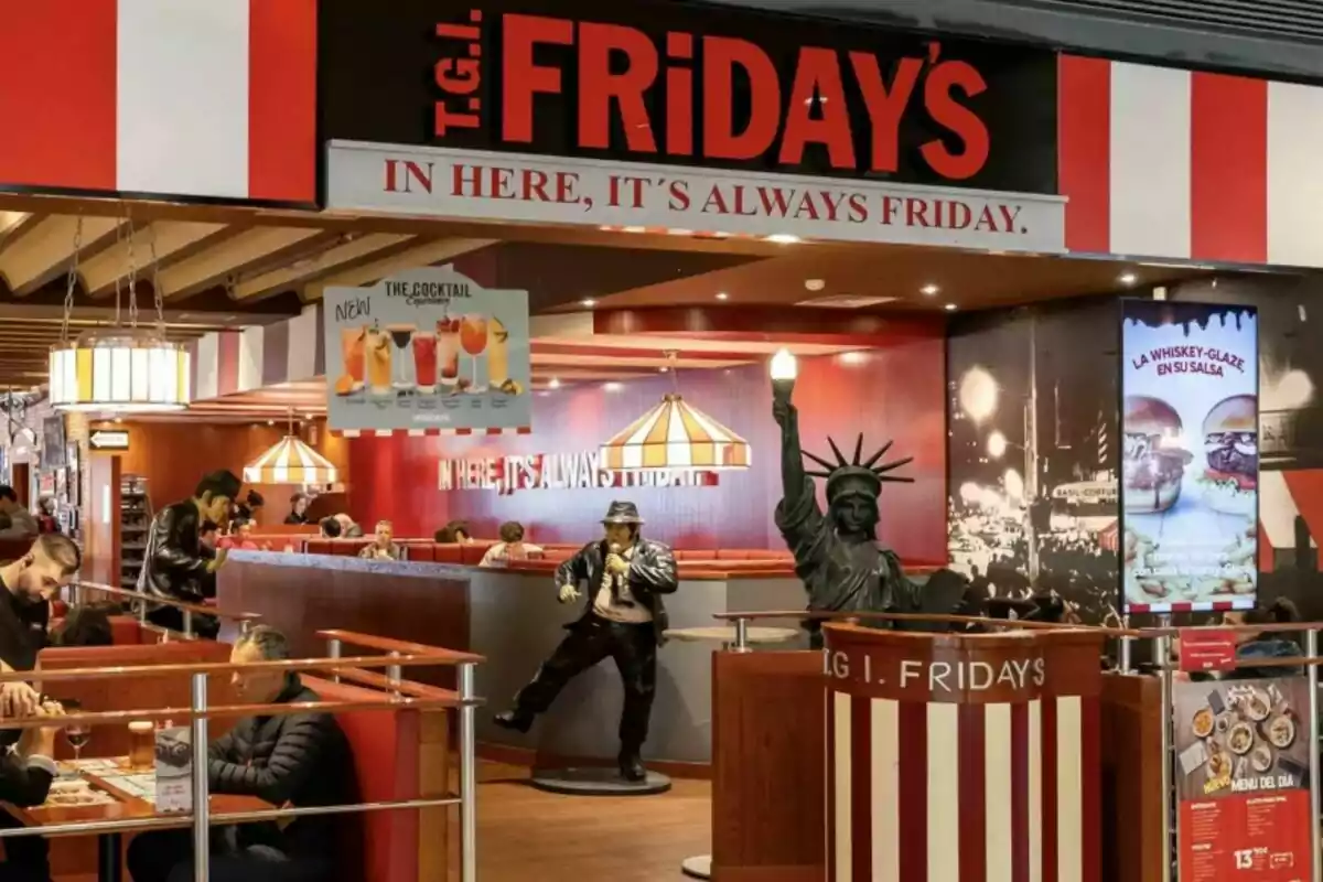 Entrance of a T.G.I. Friday's restaurant with themed decor, including a Statue of Liberty and a musician mannequin, where customers are seen sitting at tables enjoying their meals. Entrance of a T.G.I. Friday's restaurant with themed decor, including a Statue of Liberty and a musician mannequin, where customers are seen sitting at tables enjoying their meals.