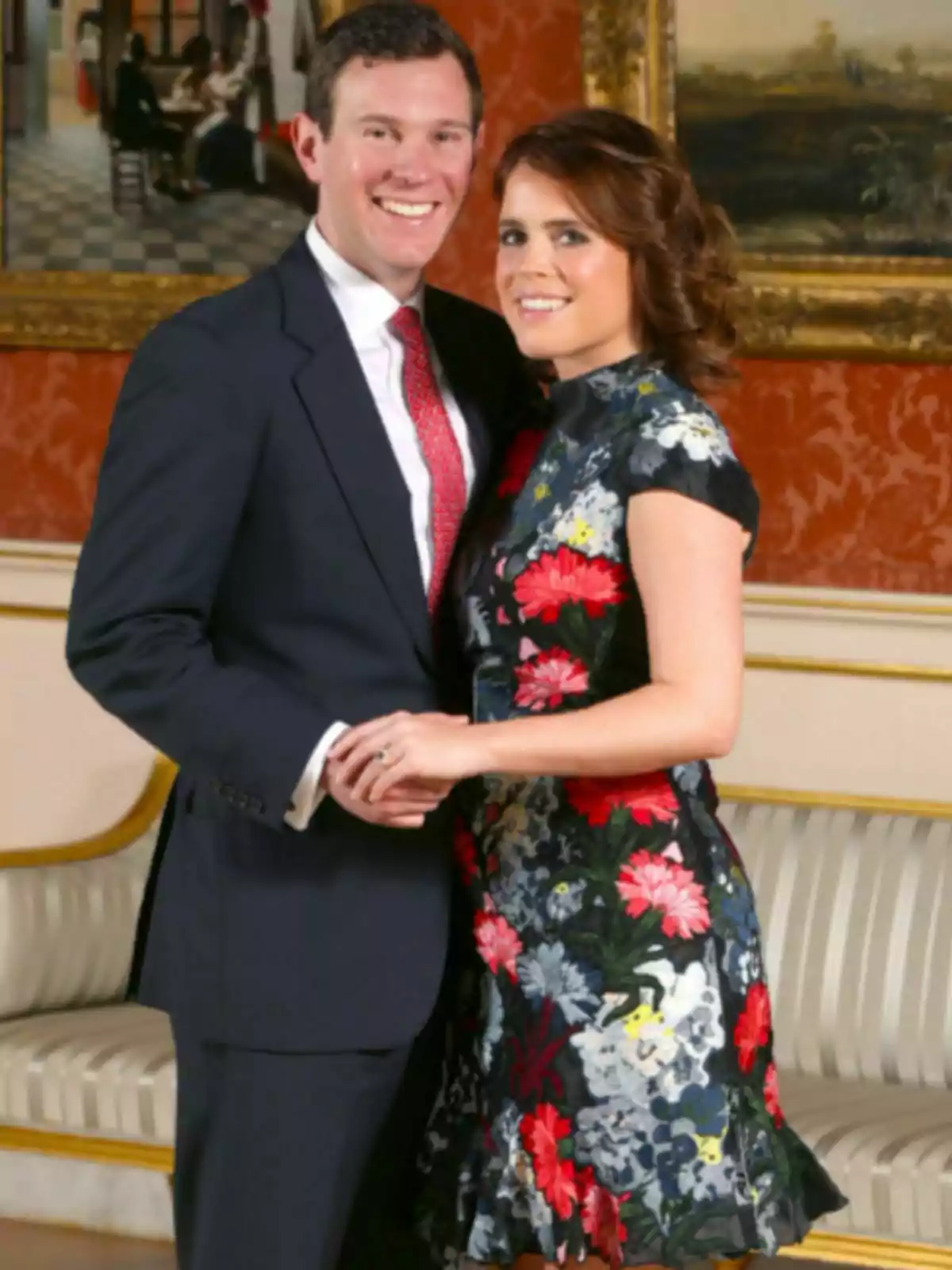 Jack Brooksbank and Princess Eugenie smile together in an elegant room with red walls and framed paintings in the background. Jack Brooksbank and Princess Eugenie smile together in an elegant room with red walls and framed paintings in the background.