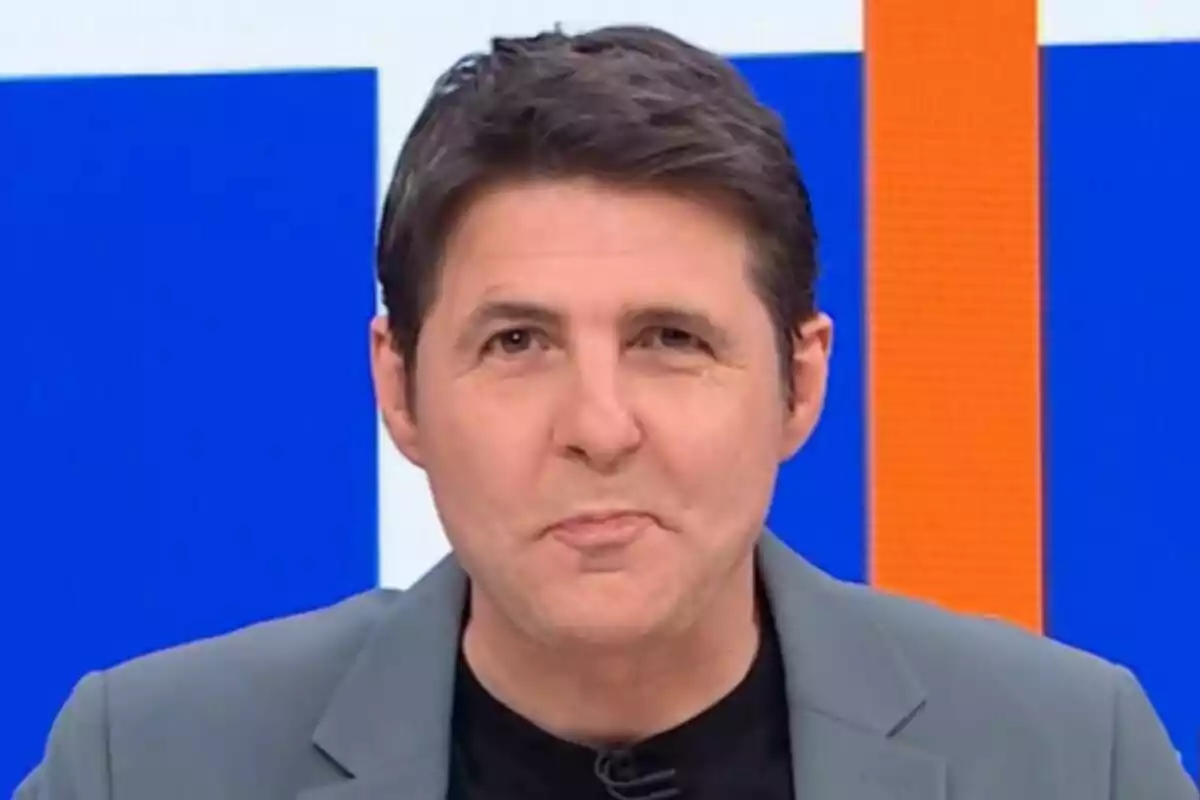 Jesús Cintora con cabello oscuro y chaqueta gris frente a un fondo azul y naranja en Malas Lenguas. Jesús Cintora con cabello oscuro y chaqueta gris frente a un fondo azul y naranja en Malas Lenguas.