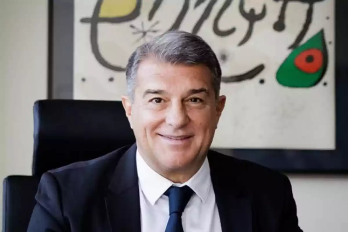A man in a suit and tie smiling in front of an abstract artwork on the wall.