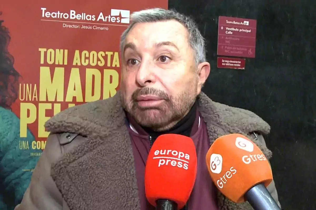 José Manuel Parada amb barba i jaqueta de llana és entrevistat per diversos mitjans de comunicació davant d'un cartell de teatre.