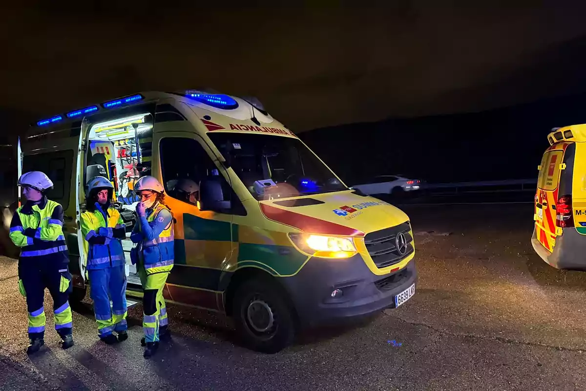 Paramèdics al costat d'una ambulància amb llums encesos en una carretera a la nit.