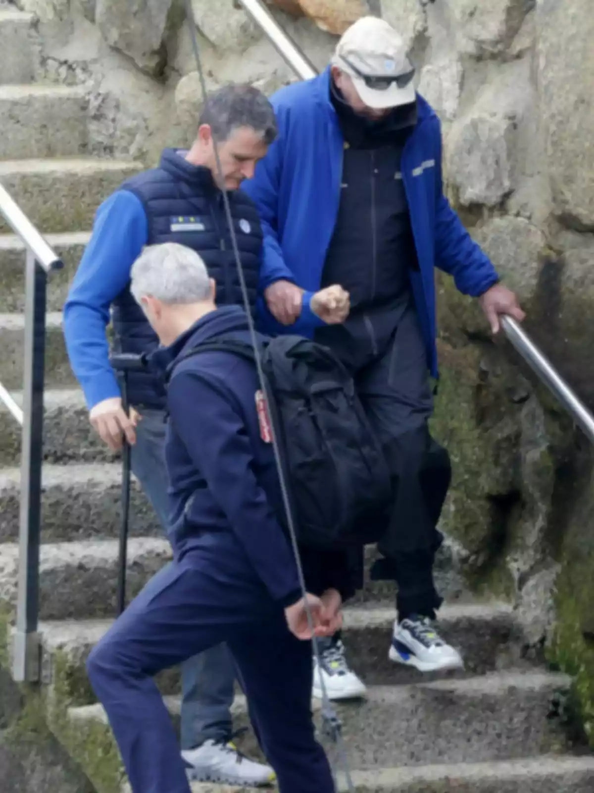 Joan Carles I, Pere Campos i un altre home baixen per unes escales de pedra a l'aire lliure, un d'ells ajuda a un altre a baixar mentre el tercer porta una motxilla i sosté un objecte llarg. Joan Carles I, Pere Campos i un altre home baixen per unes escales de pedra a l'aire lliure, un d'ells ajuda a un altre a baixar mentre el tercer porta una motxilla i sosté un objecte llarg.