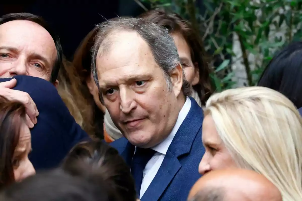 Juan Gomez Acebo wearing a blue suit and tie is surrounded by several people at an outdoor event.