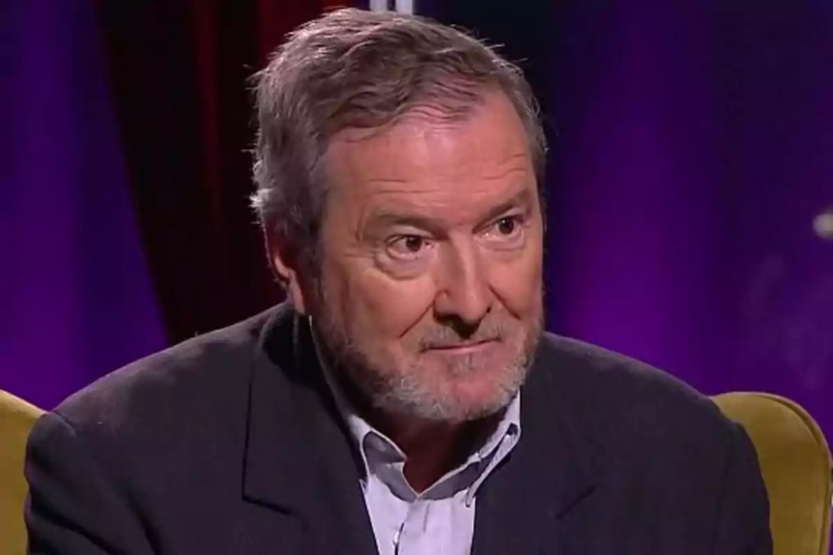 Juan José Benítez sitting in an armchair with a dark background and purple lights Juan José Benítez sitting in an armchair with a dark background and purple lights