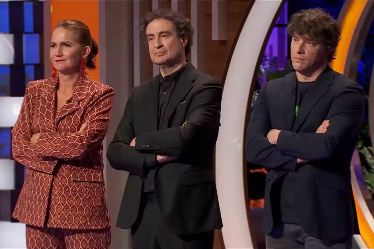 Samantha Vallejo-Nágera, Pepe Rodríguez i Jordi Cruz drets amb els braços creuats, vestits de manera formal, en un entorn il·luminat i acolorit a MasterChef. Samantha Vallejo-Nágera, Pepe Rodríguez i Jordi Cruz drets amb els braços creuats, vestits de manera formal, en un entorn il·luminat i acolorit a MasterChef.