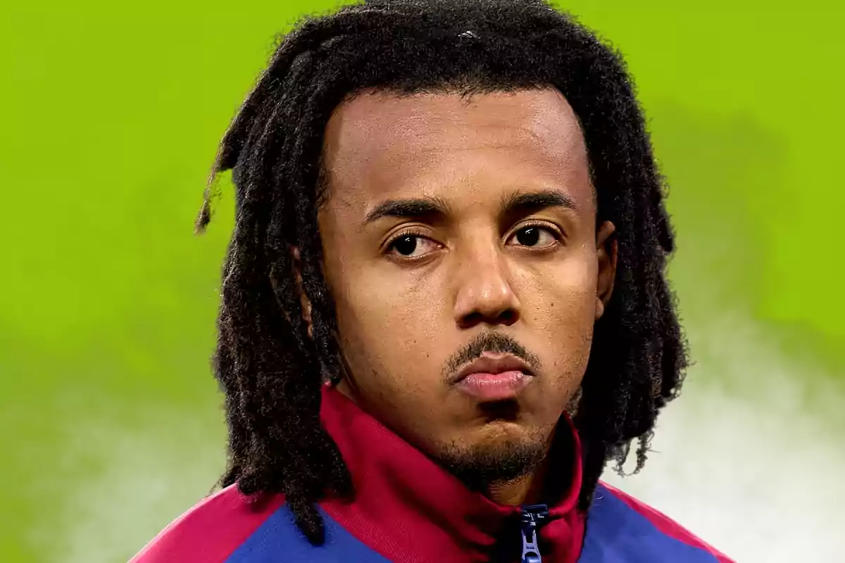 A man with dreadlocks and a sports jacket on a green background.