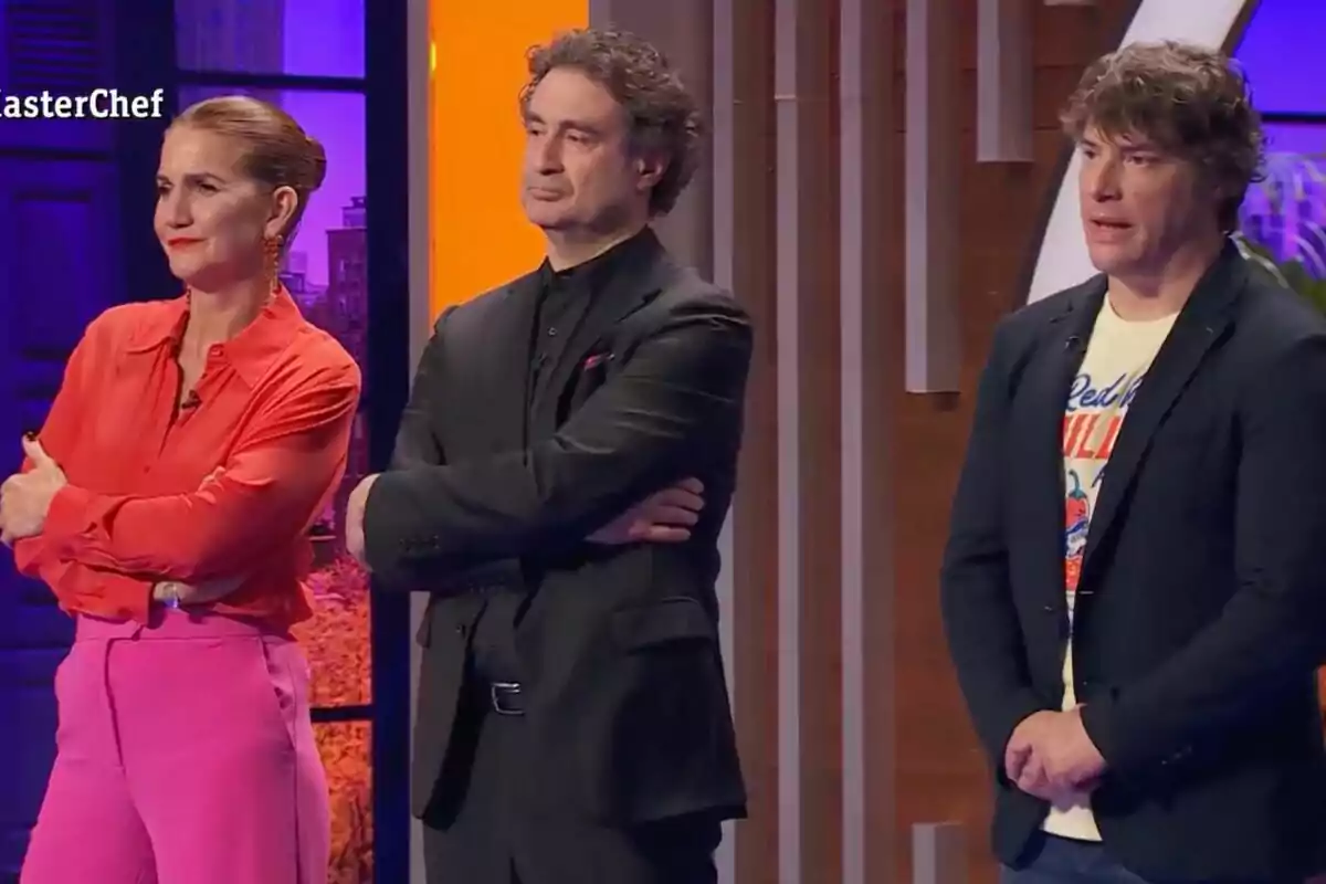 El jurado de 'Masterchef' de pie con expresiones serias en un set de televisión iluminado con luces de colores. El jurado de 'Masterchef' de pie con expresiones serias en un set de televisión iluminado con luces de colores.